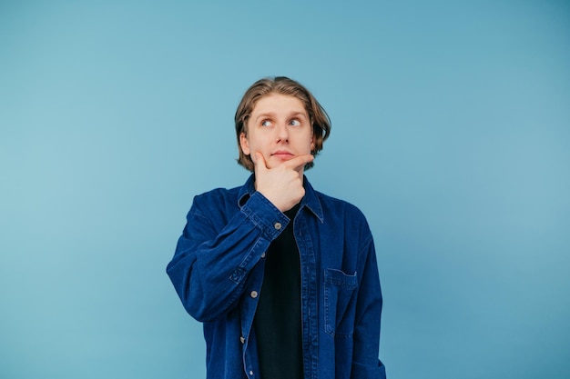 Pensive male student in a shirt stands on a blue background and looks away