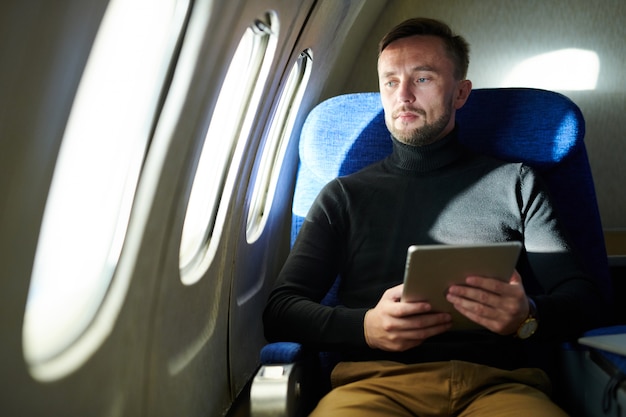 Pensive Man Holding Tablet in Airplane