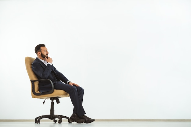 The pensive man sitting on an office chair on the white wall background