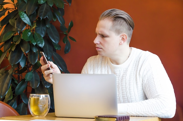 Pensive man stares looking at smartphone, remotely works on laptop, gets bad news. world economic crisis. self-isolation, bankruptcy.