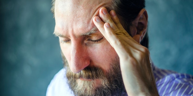 Pensive Man with a Beard Massages the Left Temple