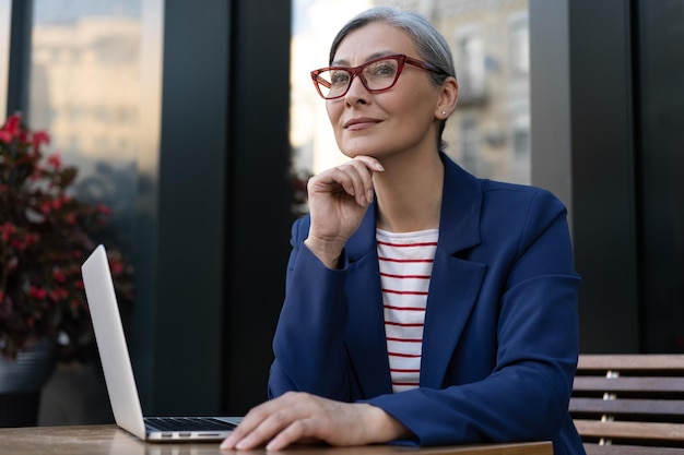 Photo pensive mature businesswoman using laptop computer working online at workplace