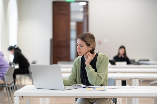 Pensive mature female student attending distance learning courses sitting at library desk