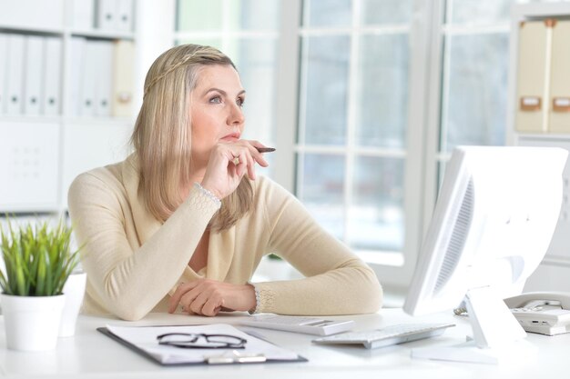 Pensive mature woman using computer and making notes