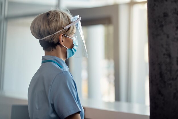 Pensive nurse with face shield and protective face at medical clinic