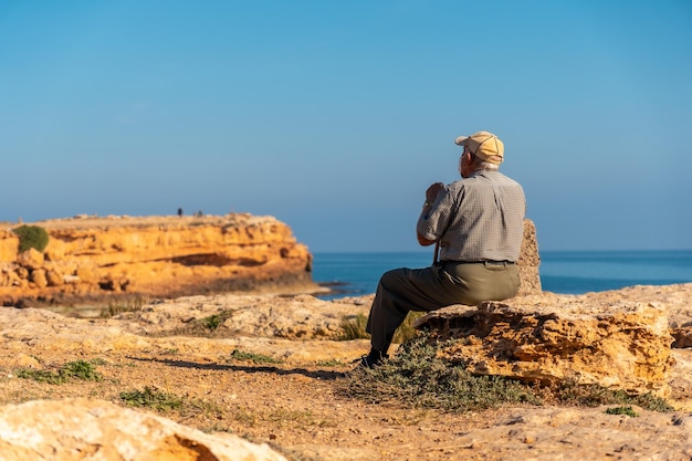 Pensive old man in a beret sitting on the shoreline by the sea Traditional lord of Spanish culture