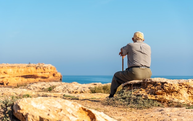 Pensive old man in beret sitting and with walking stick on the
shore by the sea traditional lord of spanish culture