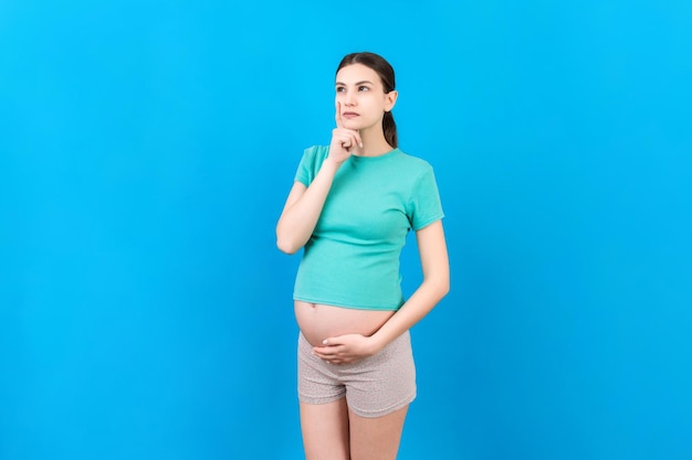 Donna incinta pensierosa che sceglie il nome per il bambino su sfondo colorato sogno e donna incinta felice che pensa immaginando lo spazio della copia della vita della maternità