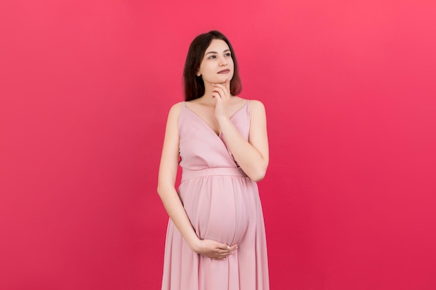 Pensive pregnant woman choosing name for baby on colored background Dream and Happy Pregnant Woman Thinking Imagining Motherhood Life Copy Space