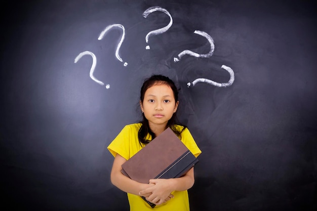 Pensive schoolgirl with books and question marks