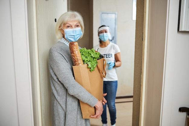 Pensive senior woman and a young caretaker standing behind her