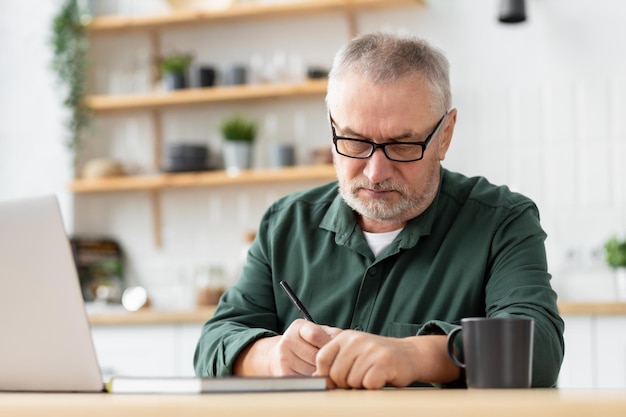 Pensive serious elderly man with laptop sitting at table check finances at home