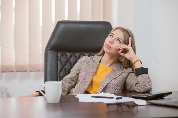 Pensive serious woman boss sitting at the table in her office