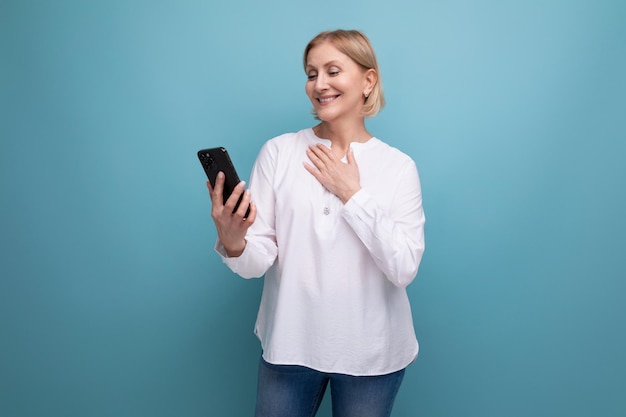 Pensive slender blondie middleaged woman in a white blouse masters the smartphone gadget