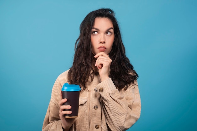 pensive smart millennial european woman student with cup of coffee takeaway thinks look at empty space