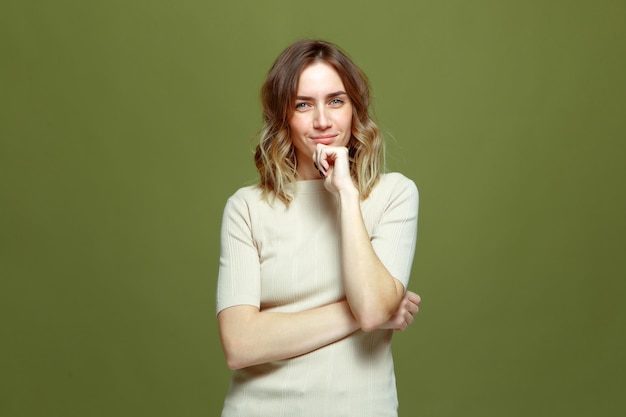 Pensive smiling young female with beautiful face looking at camera on green studio background