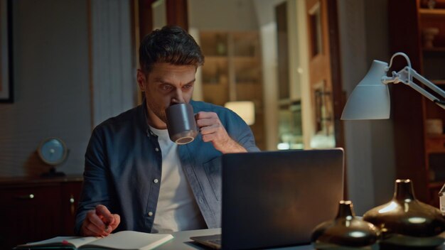 Foto startup pensieroso che beve il tè di notte casa ufficio closeup ragazzo con la penna