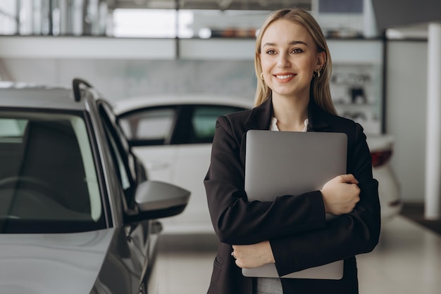 Pensive stylish businesswoman manager in suit holding laptop computer standing near car