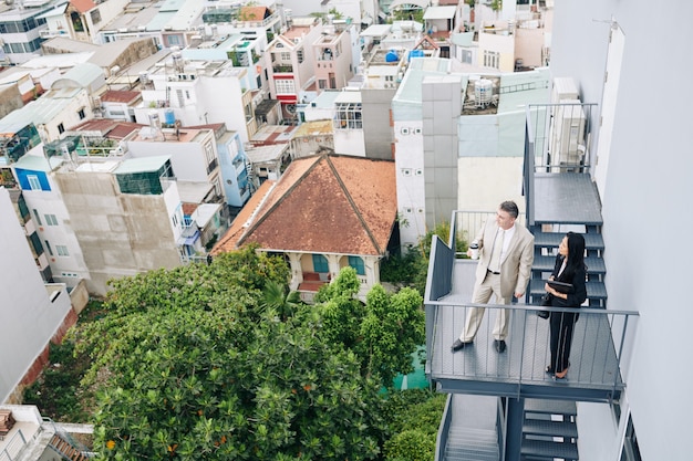 Pensive successful entrepreneurs standing on fire escape staircase looking at city during coffee break