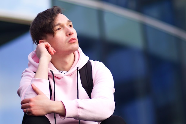 Pensive thought sad young man is sitting outdoors and looking into distance