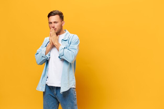 Pensive thoughtful tanned handsome man in blue basic tshirt\
fold hands look at camera posing isolated on yellow studio\
background copy space banner mockup people emotions lifestyle\
concept