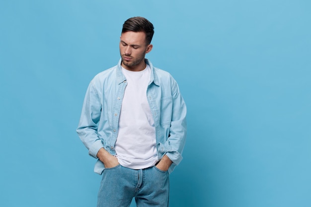 Pensive upset thoughtful tanned handsome man in casual basic\
tshirt hold hands on jeans pocket posing isolated on blue studio\
background copy space banner mockup people emotions lifestyle\
concept