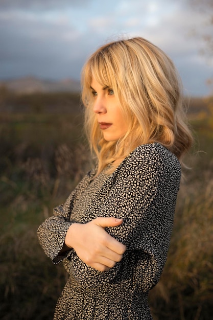 Pensive woman in dress standing in gloomy countryside