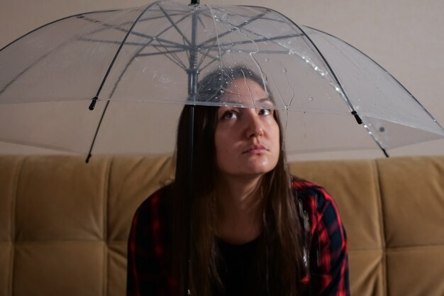 Pensive woman hides from flowing water under clear umbrella