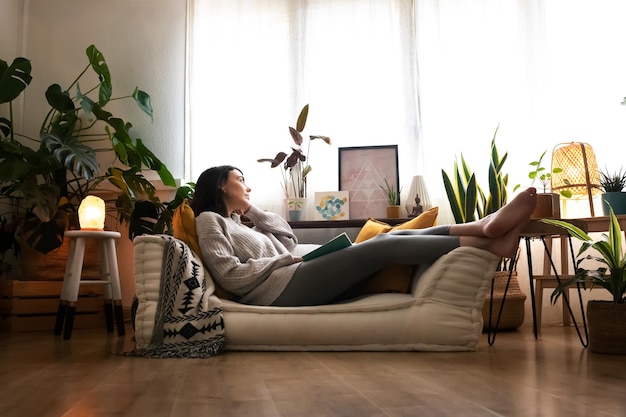 Pensive woman relaxes at home lying on sofa looking out the window. Copy space. Lifestyle concept.