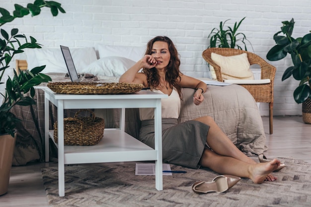 Pensive woman sits on the floor with a laptop at home