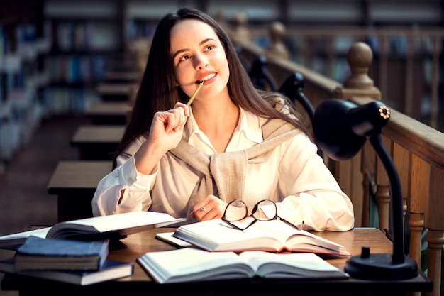 Pensive woman sitting at the library and thinking with pencil at the mouthe