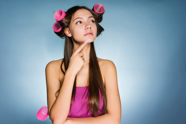 Pensive woman with curlers on head on blue background