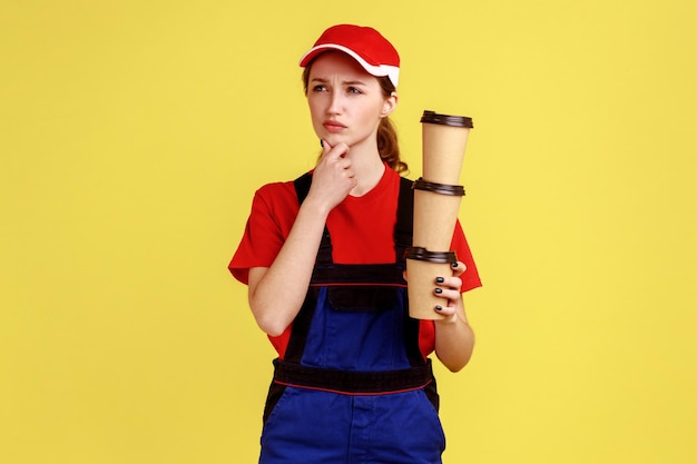 Pensive worker woman standing with stack of disposable cups thinking holding chin and looking away