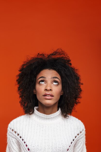 Pensive young african woman wearing casual clothes standing isolated over red wall, looking up