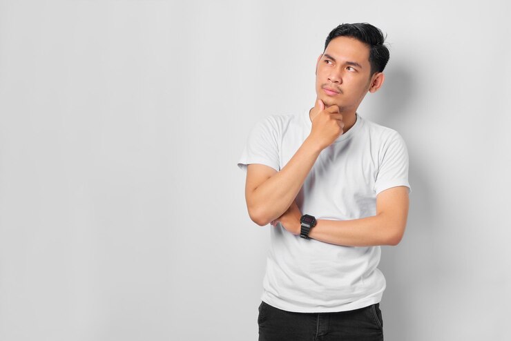白い背景で隔離の紛らわしいアイデアについて思慮深い質問を考えて真面目な顔を持つ物思いにふける若いアジア人