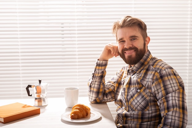 物思いにふける若いひげを生やした男性実業家のブラインドの概念の背景にコーヒーを飲む