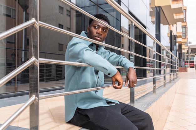 Pensive young black guy sitting near building entrance on street