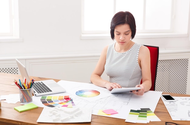 Pensive young female designer in casual working with color palette in modern workplace interior, copy space