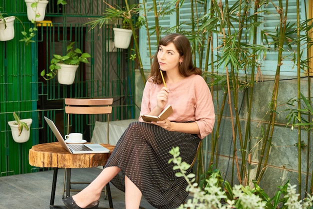 彼女の家の裏庭でコーヒーを飲むときに新しい本のアイデアについて熟考している物思いにふける若い女性作家