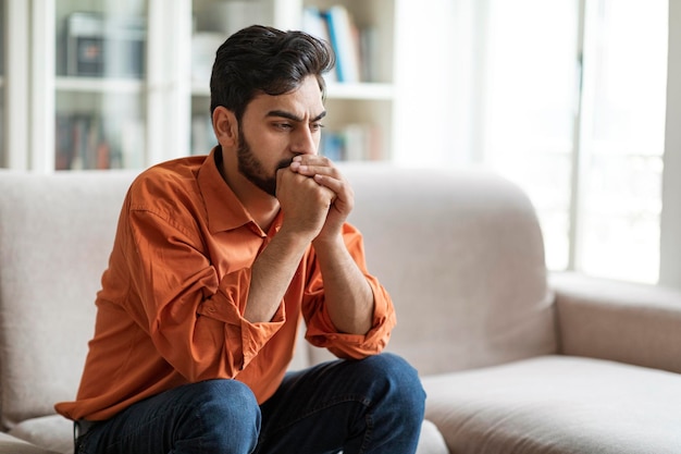 Pensive young middle eastern man sitting on sofa at home