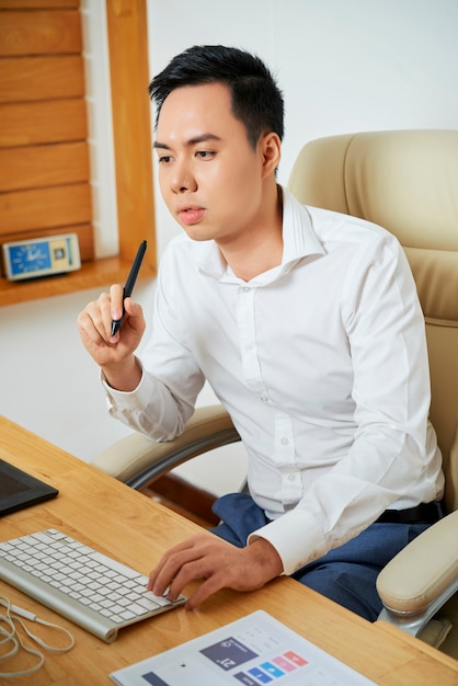 Pensive young ux designer working on computer at his office desk and creating new design