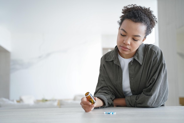 Pensive young woman holds bottle with medicines doubt whether to take pills Healthcare Copy space