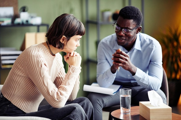 Pensive young woman listening to psychotherapist explaining how to recover from traumatizing experience