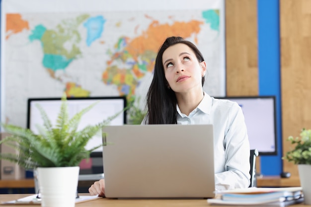 Pensive young woman sits at laptop and looks up