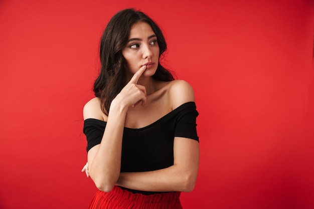 Pensive young woman wearing a dress standing isolated over red