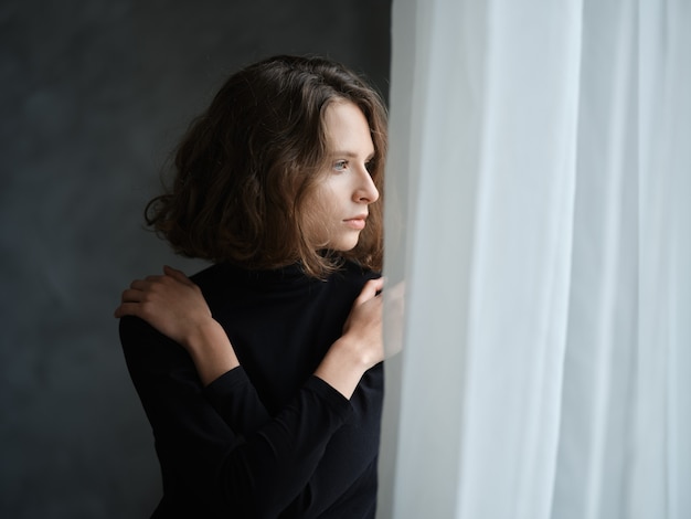 Pensive young woman with curly hair near the window