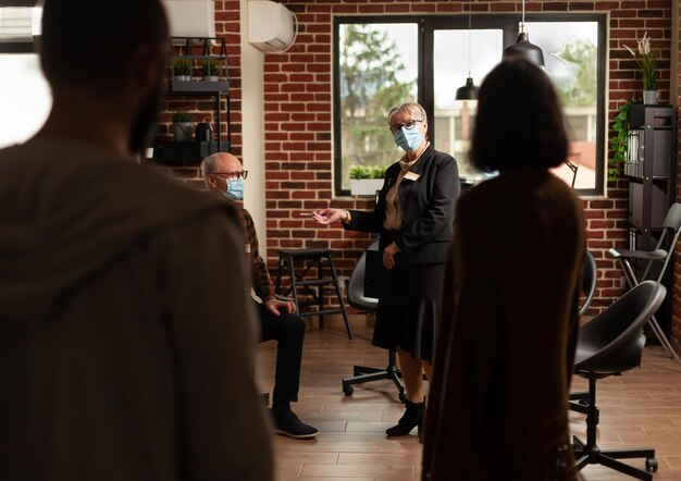 People at aa group meeting standing in office to do mental health exercise with therapist. Patients attending therapy session program to receive counseling from psychotherapist during pandemic.