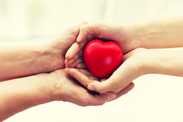 people, age, family, love and health care concept - close up of senior woman and young woman hands holding red heart