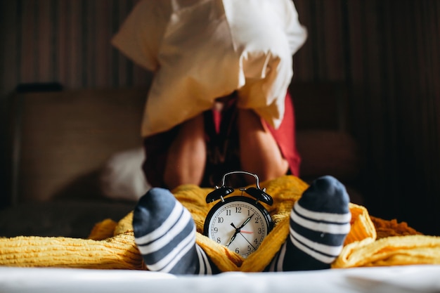 People are awakened from sleep by the alarm clock showing 7 oclock and cover their ears with pillows