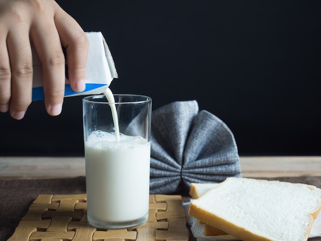 Photo people are pouring milk in a box on clear glass.